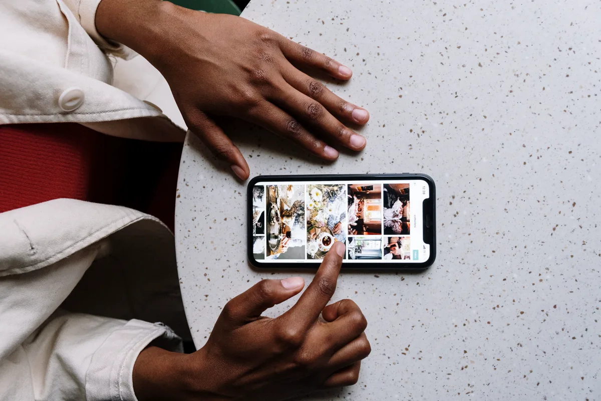 Hands scrolling a photo grid on a smartphone on a speckled cafe table