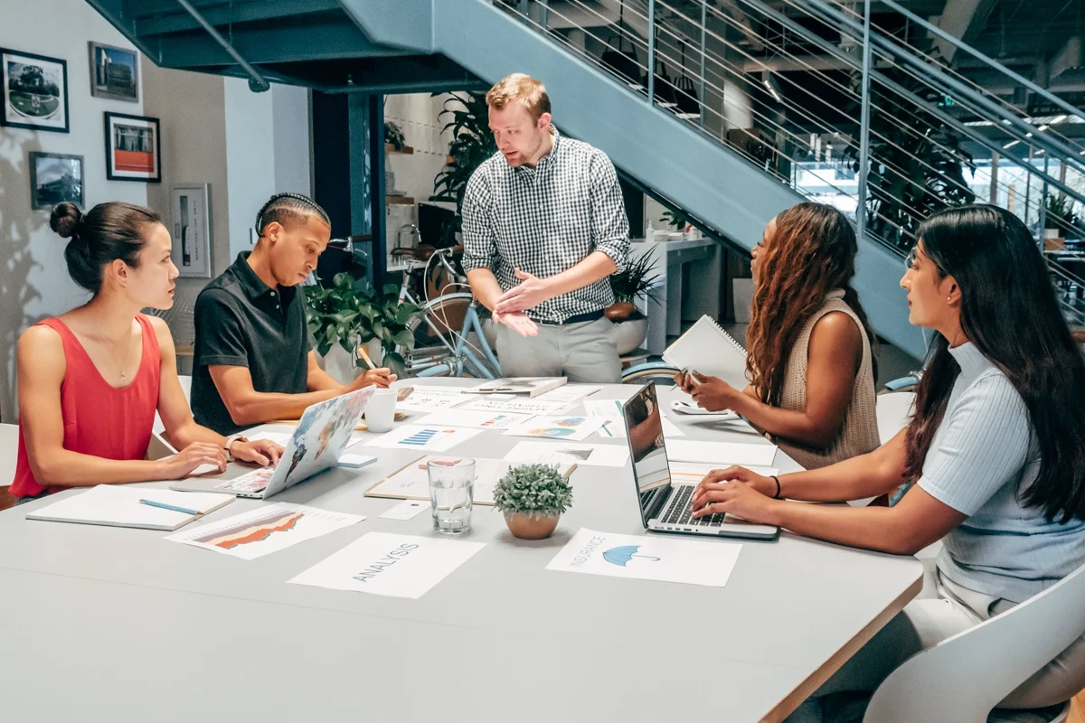 Diverse colleagues collaborating at a conference table with laptops and printed charts in a modern office