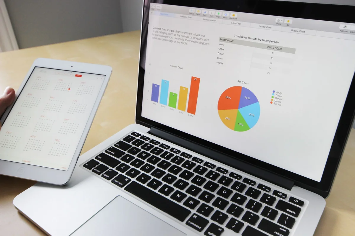 Laptop displaying charts and graphs with tablet and calendar on a white desk for data analysis